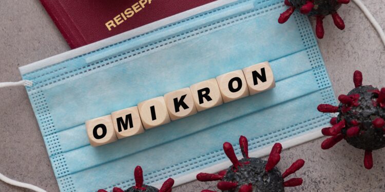 Würfel mit Buchstaben, die das Wort "OMIKRON" bilden, liegen auf einer Mund-Nasen-Schutzmaske.