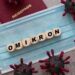 Würfel mit Buchstaben, die das Wort "OMIKRON" bilden, liegen auf einer Mund-Nasen-Schutzmaske.