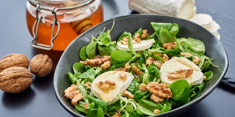 Teller mit Feldsalat mit Ziegenkäse und Walnüssen neben einem Glas Honig und einer Ziegenkäserolle