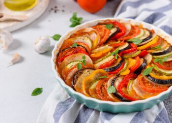 Ein mediterraner Kartoffelauflauf mit Gemüse ist in einer weißen Schale angerichtet.