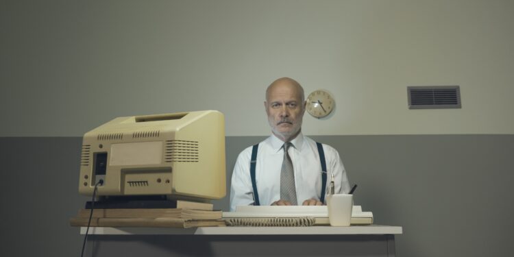 Ein ordentlich gekleideter Mann sitzt an einem Schreibtisch in einem Büro.