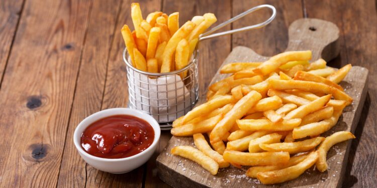 Eine Portion Pommes frites ist auf einem Holzbrett angerichtet.