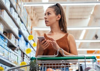 Eine Frau im Supermarkt mit einem Smartphone in der Hand.