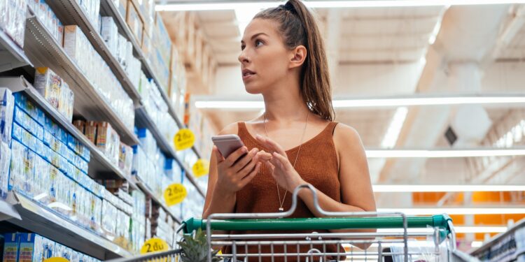 Eine Frau im Supermarkt mit einem Smartphone in der Hand.