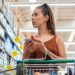 Eine Frau im Supermarkt mit einem Smartphone in der Hand.