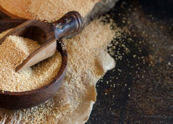 Rohes Amaranth-Korn in einer Holzschale mit einem Holzlöffel auf einem dunklen Tisch