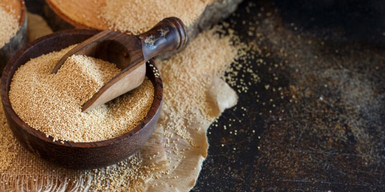 Rohes Amaranth-Korn in einer Holzschale mit einem Holzlöffel auf einem dunklen Tisch