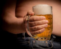 Ein Mann hält ein großes Glas Bier vor seinen Bauch.