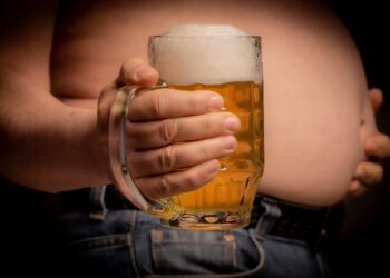 Ein Mann hält ein großes Glas Bier vor seinen Bauch.