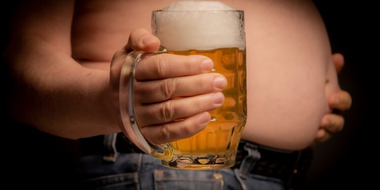 Ein Mann hält ein großes Glas Bier vor seinen Bauch.