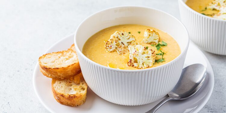 Eine Portion Blumenkohl-Suppe ist in einer weißen Suppenschüssel angerichtet.