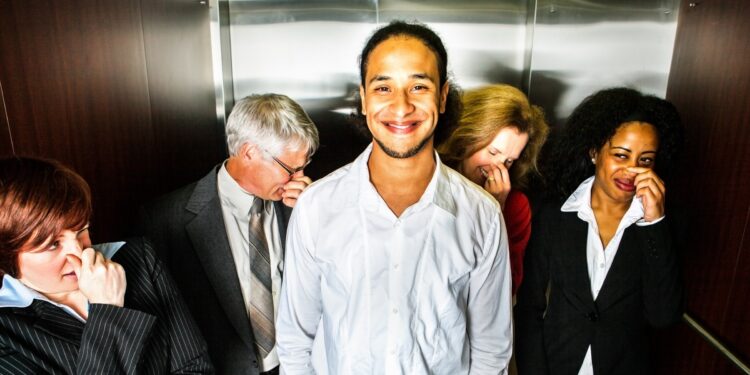 Fünf Personen im Fahrstuhl: Eine grinst und vier halten sich die Nase zu.