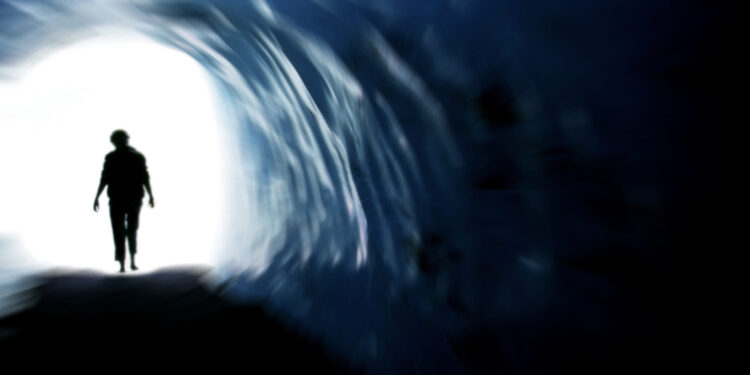 Mensch geht am Ende eines dunklen Tunnels ins Licht.