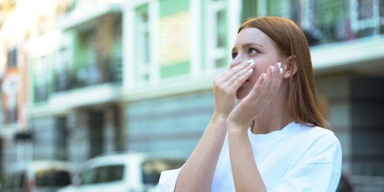 Eine Frau steht auf der Straße und hält sich die Nase zu.