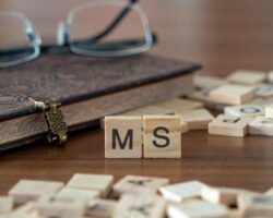 Die Buchstaben MS auf Holzstücken vor einem Buch und einer Brille