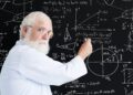 Eine älterer Mann schreibt mathematische Gleichungen an eine Tafel.