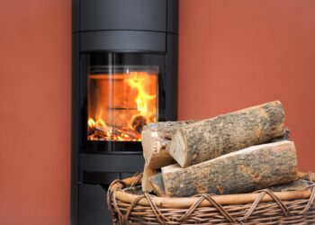 Holz in einem Korb vor einem Kaminofen, in dem ein Feuer brennt