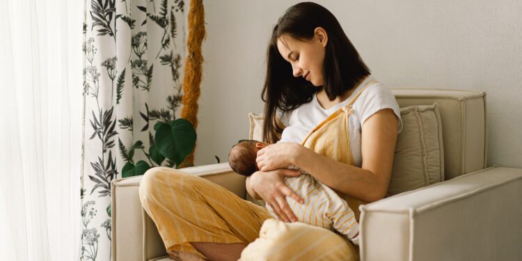 Frau sitzt lächelnd in einem Sessel und stillt ihr Baby