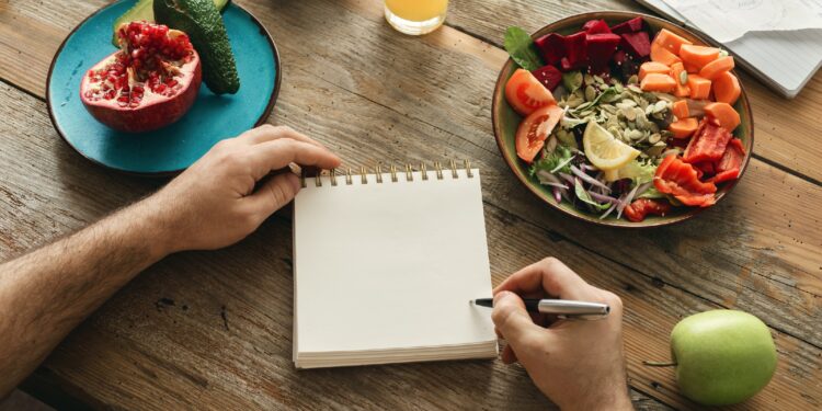 Mann mit Notizblock und Stift in der Hand beim gesunden Essen