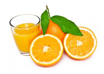 Eine aufgeschnittene Orange liegt neben einem Glas mit Organgensaft.