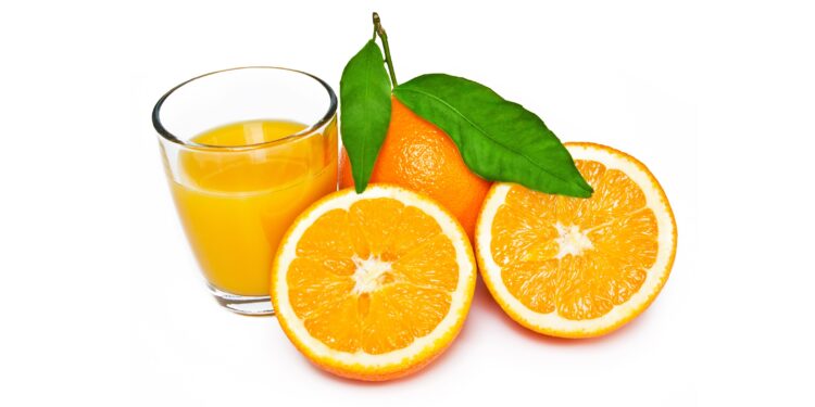 Eine aufgeschnittene Orange liegt neben einem Glas mit Organgensaft.