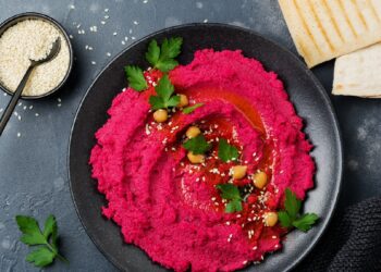 Eine Portion Rote Beete-Hummus ist in einer schwarzen Schüssel angerichtet.