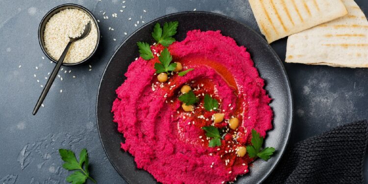 Eine Portion Rote Beete-Hummus ist in einer schwarzen Schüssel angerichtet.