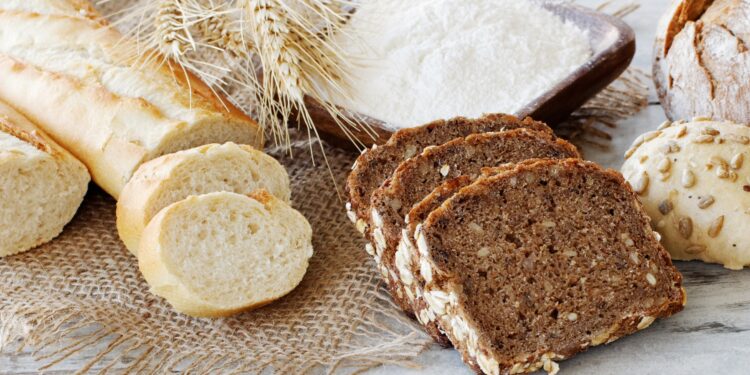 Ein Weißbrot und einige Scheiben Vollkornbrot liegen auf einer hölzernen Oberfläche.