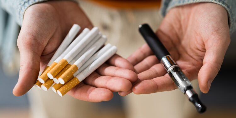 Das Bild zeigt zwei Hände: In einer Hand liegen Zigaretten und in der anderen eine E-Zigarette.