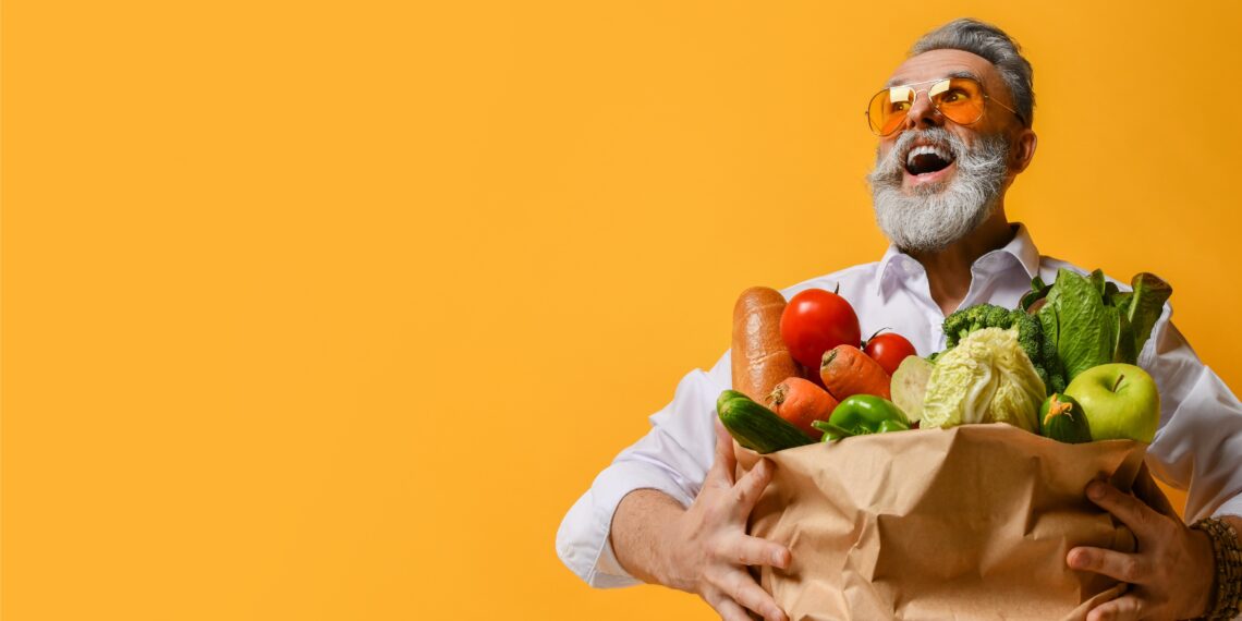 Ein Mann hält einer Einkaufstüte voller Gemüse in beiden Händen.