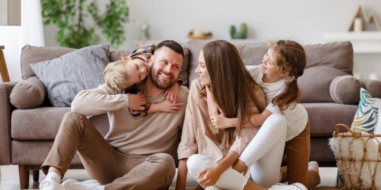 Fröhliche Eltern sitzen mit zwei Kindern vor dem Sofa