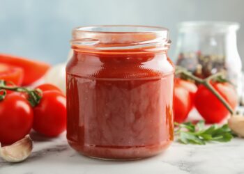 Ein Einmachglas mit selbstgemachtem Ketchup steht auf einer weißen Oberfläche.