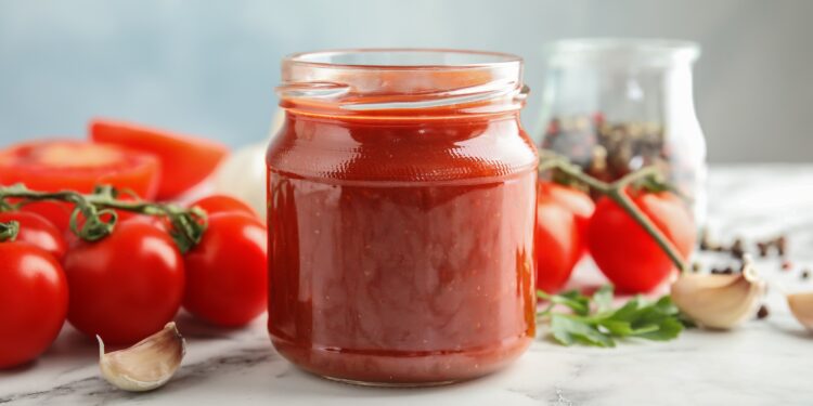 Ein Einmachglas mit selbstgemachtem Ketchup steht auf einer weißen Oberfläche.