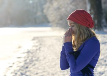 Eine junge Frau steht im Schnee und putzt sich die Nase.