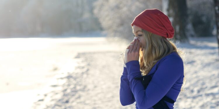 Eine junge Frau steht im Schnee und putzt sich die Nase.