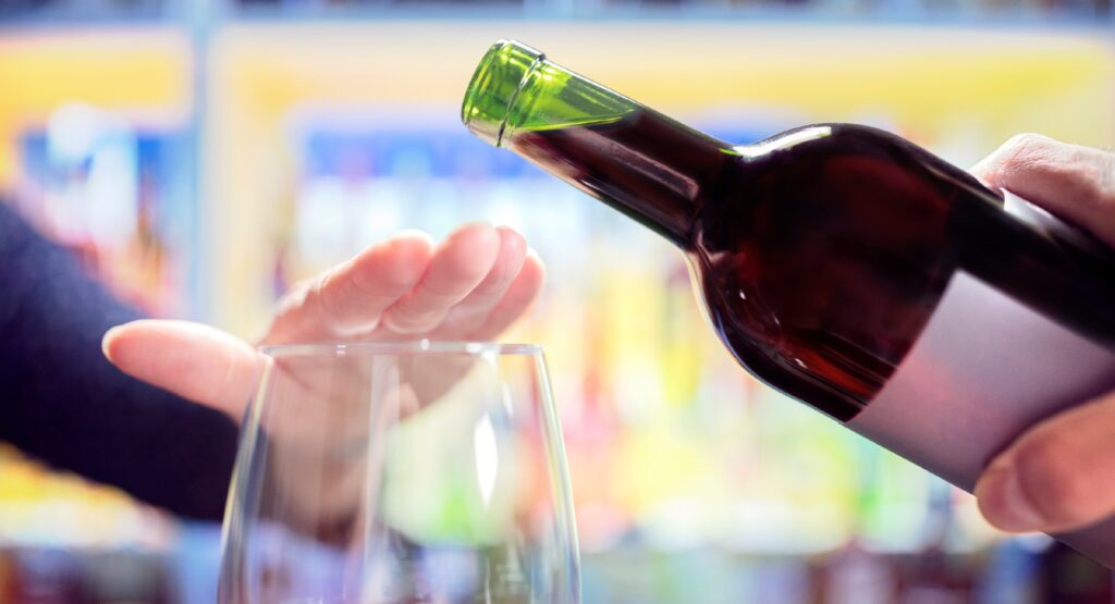 Eine Frau macht eine abweisende Geste mit ihrer Hand, als ihr Wein angeboten wird.