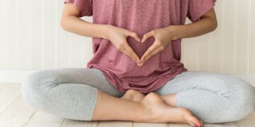 Eine Person sitzt im Schneidersitz auf den Boden und formt mit beiden Händen ein Herz vor dem Bauch.