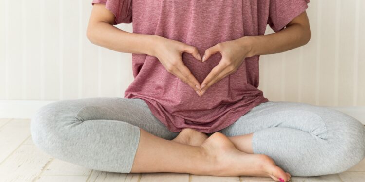 Eine Person sitzt im Schneidersitz auf den Boden und formt mit beiden Händen ein Herz vor dem Bauch.