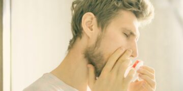 Junger Mann hält sich Taschentuch an blutende Nase