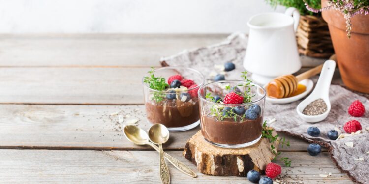 Zwei Portionen Chia-Schokoladen-Pudding sind auf einer hölzernen Oberfläche angerichtet.