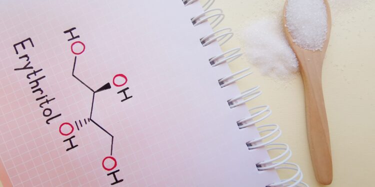 Ein Löffel mit Süßstoff liegt neben einem Stück Papier, auf dem die chemische Formel für Erythritol geschrieben steht.