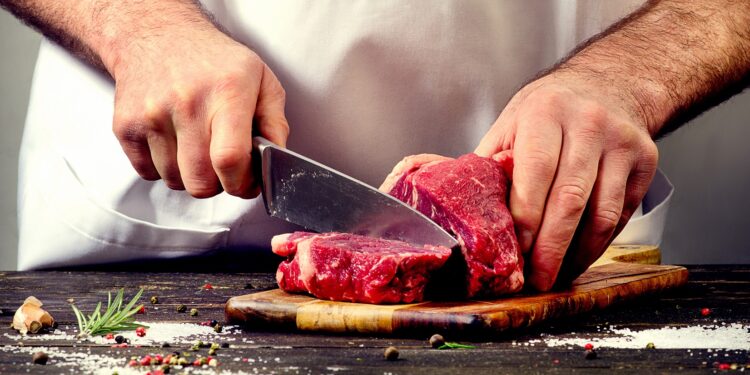 Ein Mann schneidet ein Stück Fleisch auf einem Holzbrett.