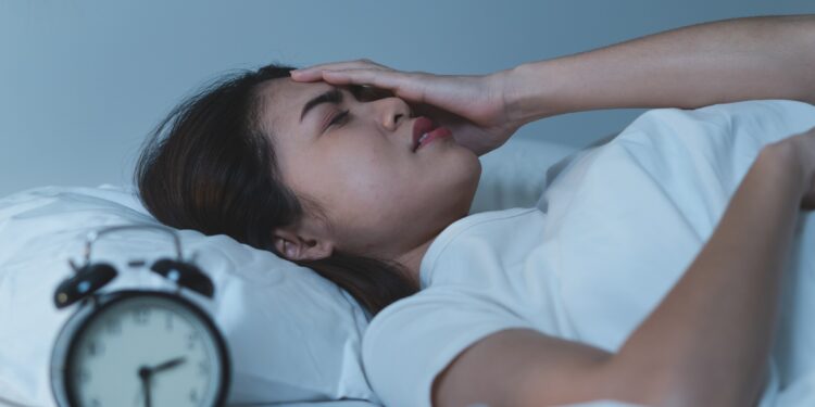 Im Bett liegende junge asiatische Frau hält sich die Hand an den Kopf