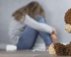 Ein Teddy sitzt neben einem traurigen Mädchen.