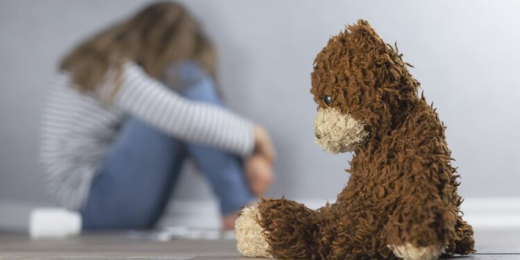 Ein Teddy sitzt neben einem traurigen Mädchen.
