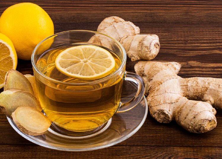 Eine Tasse mit frischem Ingwertee steht auf einer hölzernen Oberfläche.