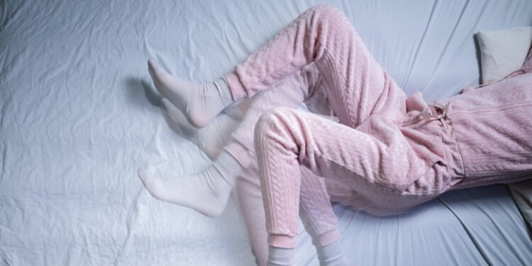 Eine Frau mit unruhigen Beinen liegt in einem Bett.