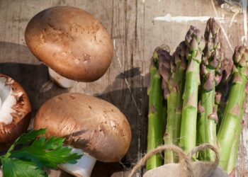 Ein Bund Spargel und einige Champignons liegen auf einer hölzernen Oberfläche.