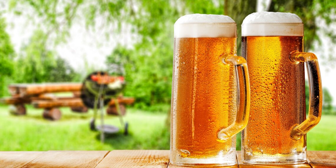 Zwei mit Bier gefüllte Gläser auf einem Tisch vor einem Grill im Freien.