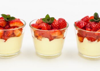 Panna cotta mit Erdbeeren in drei Gläsern vor weißem Hintergrund.